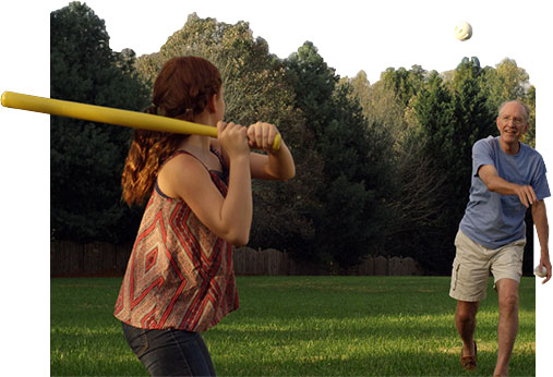 A grandfather and granddaughter playing ball on a lush green lawn
